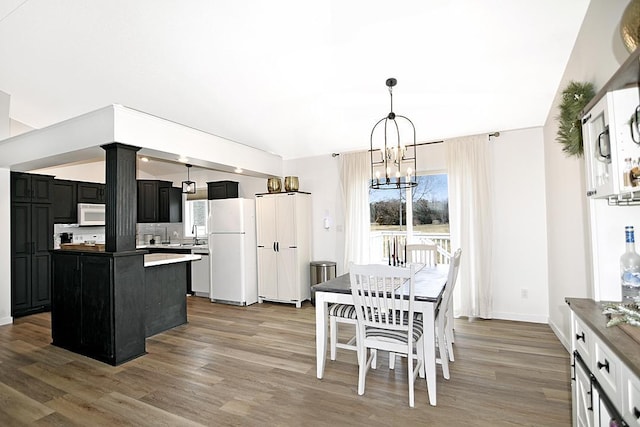 kitchen featuring a notable chandelier, a kitchen island, wood finished floors, dark cabinets, and white appliances