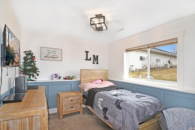 bedroom featuring wainscoting, carpet flooring, visible vents, and a decorative wall