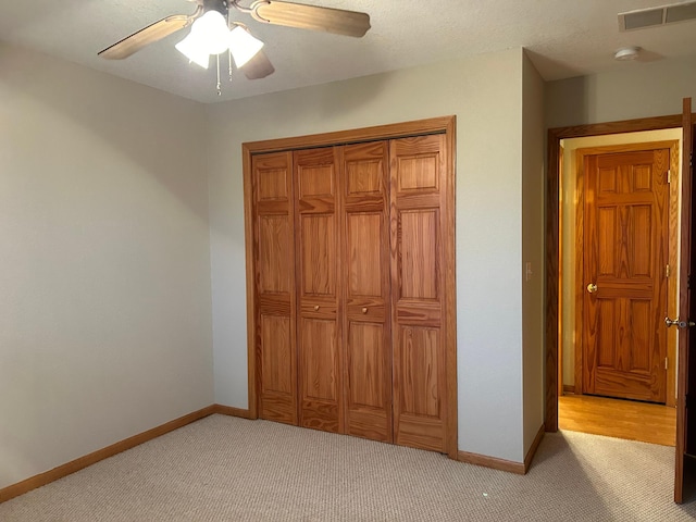 unfurnished bedroom featuring a textured ceiling, a closet, ceiling fan, and light colored carpet