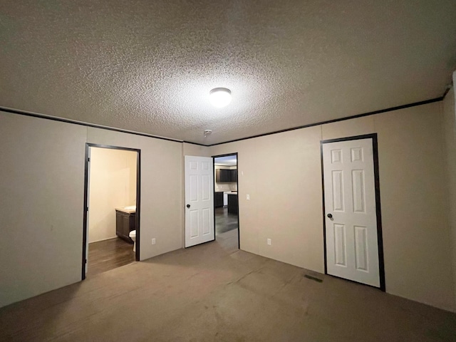 unfurnished bedroom featuring ensuite bath, carpet, and a textured ceiling