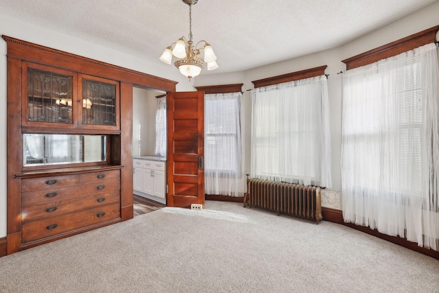 interior space featuring carpet flooring, radiator heating unit, a textured ceiling, and an inviting chandelier