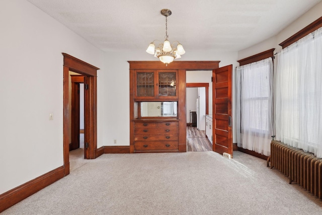 carpeted spare room with a notable chandelier, radiator heating unit, and a textured ceiling