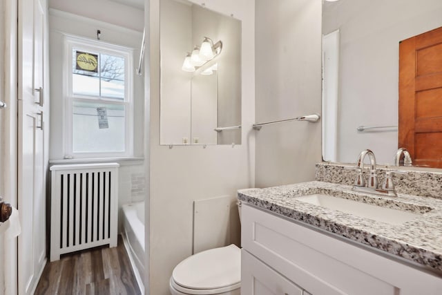 bathroom with radiator, a washtub, hardwood / wood-style floors, toilet, and vanity