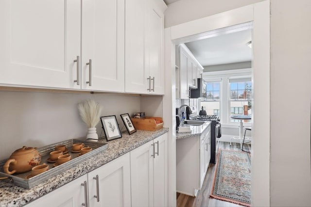 kitchen featuring light stone countertops, wood-type flooring, stainless steel gas stove, and white cabinetry