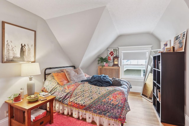 bedroom featuring a textured ceiling, light hardwood / wood-style flooring, and lofted ceiling