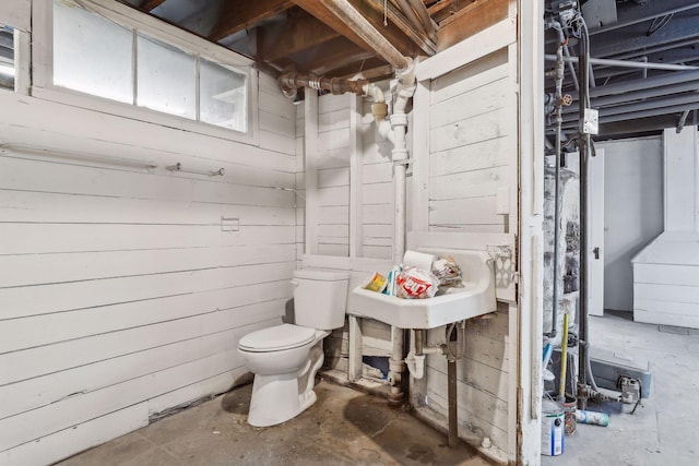 bathroom with toilet, concrete flooring, and wood walls