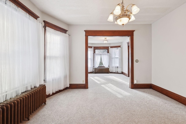 carpeted spare room featuring radiator heating unit, a notable chandelier, and a textured ceiling