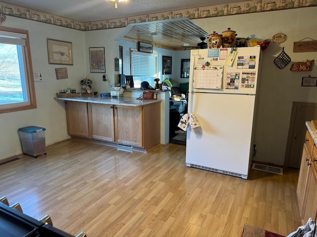 kitchen with light wood-type flooring, white refrigerator, kitchen peninsula, and light stone counters