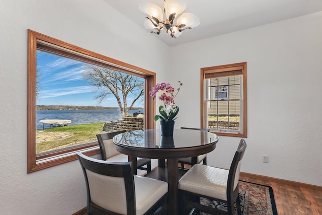 dining space with baseboards, a water view, wood finished floors, and a chandelier