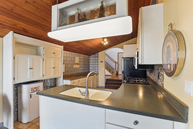 kitchen with white cabinets, dark countertops, a sink, backsplash, and wood ceiling
