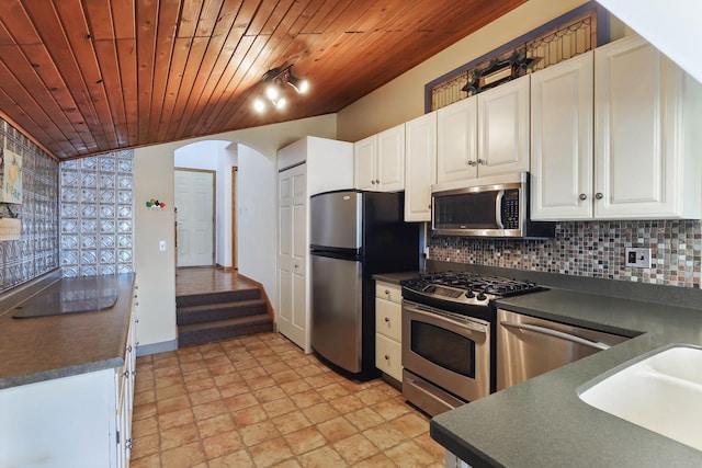 kitchen with dark countertops, appliances with stainless steel finishes, arched walkways, white cabinetry, and decorative backsplash