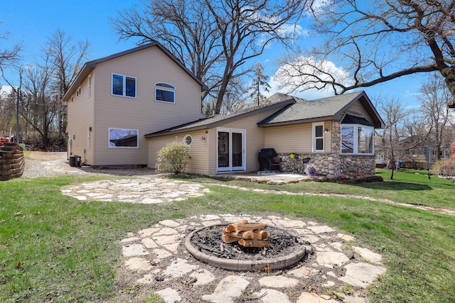 back of house featuring central AC unit, a fire pit, a yard, and stone siding