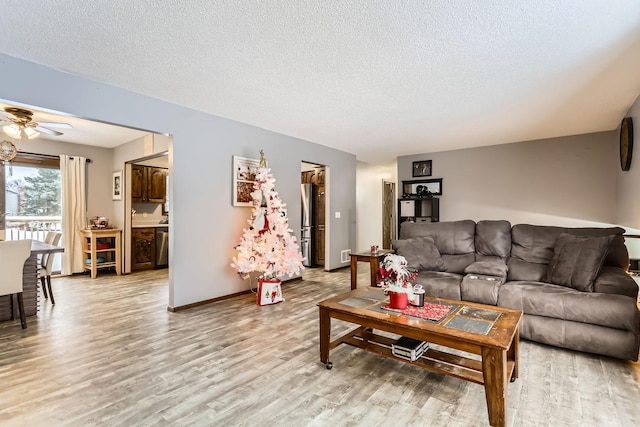 living room with ceiling fan, light hardwood / wood-style floors, and a textured ceiling