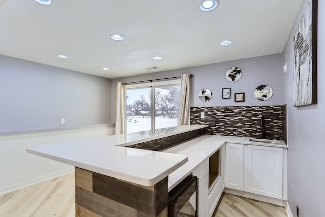 kitchen featuring kitchen peninsula, light wood-type flooring, backsplash, sink, and white cabinets