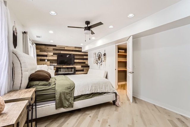 bedroom featuring light hardwood / wood-style floors, ceiling fan, wood walls, and a walk in closet