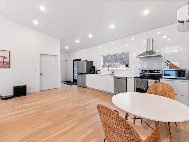 kitchen with stainless steel appliances, white cabinetry, light hardwood / wood-style floors, and wall chimney range hood