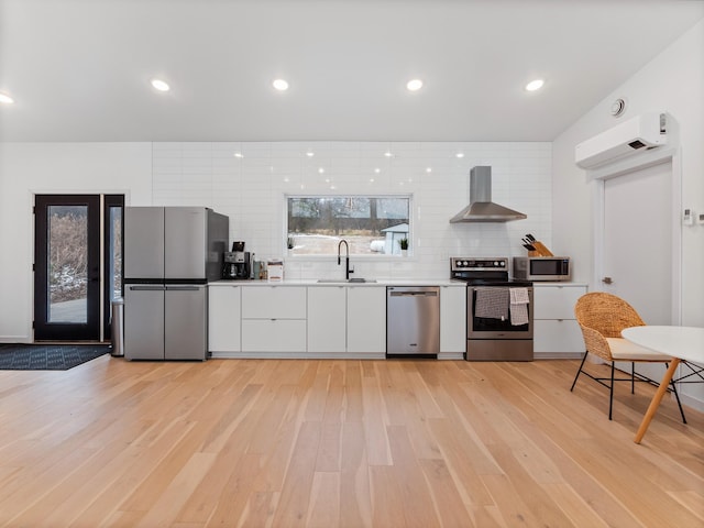 kitchen featuring sink, wall chimney exhaust hood, decorative backsplash, appliances with stainless steel finishes, and light wood-type flooring