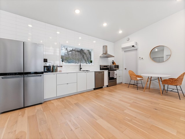 kitchen with wall chimney exhaust hood, stainless steel appliances, a wall mounted air conditioner, light hardwood / wood-style flooring, and white cabinets