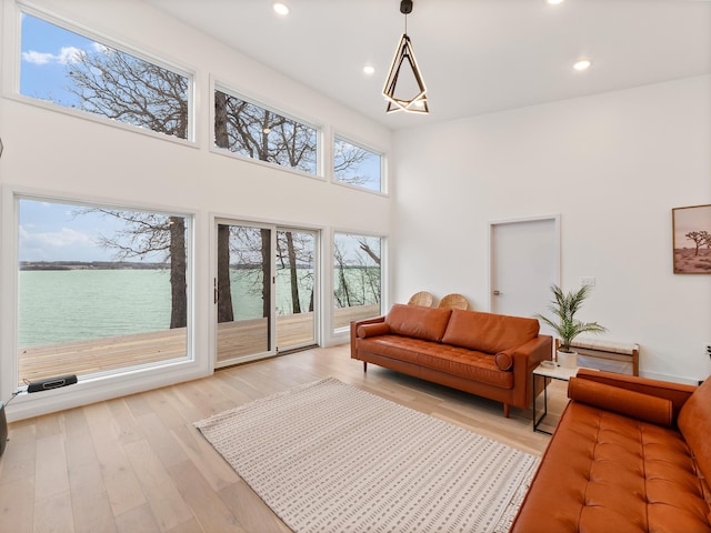 living room with a towering ceiling, light wood-type flooring, a water view, and an inviting chandelier