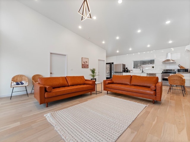 living room with light wood-type flooring, sink, high vaulted ceiling, and a chandelier