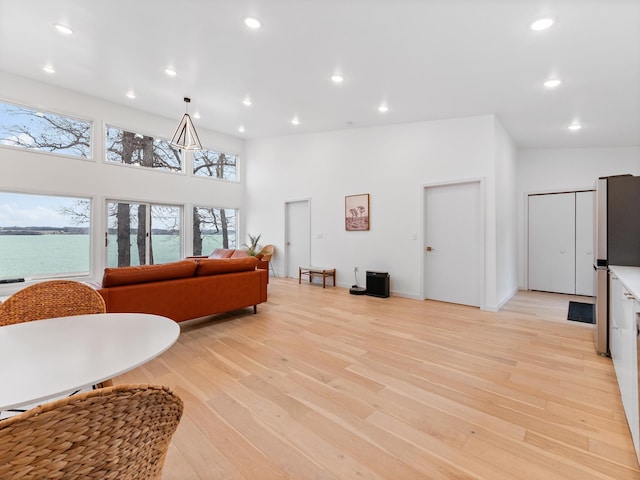 living room with a water view, a towering ceiling, and light hardwood / wood-style flooring