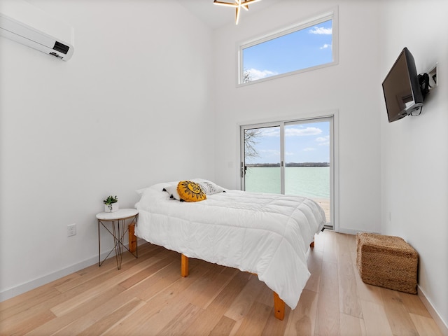 bedroom featuring an AC wall unit, a towering ceiling, and light hardwood / wood-style flooring