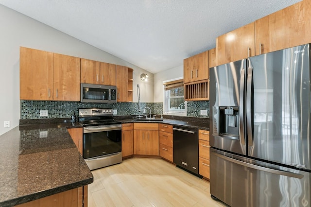 kitchen with appliances with stainless steel finishes, tasteful backsplash, dark stone counters, sink, and lofted ceiling