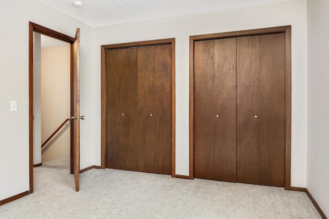 unfurnished bedroom with two closets, light colored carpet, and a textured ceiling