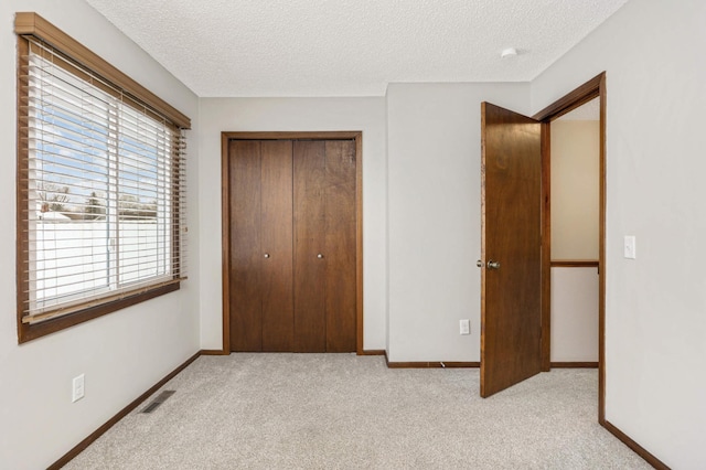 unfurnished bedroom featuring a textured ceiling, a closet, and light carpet