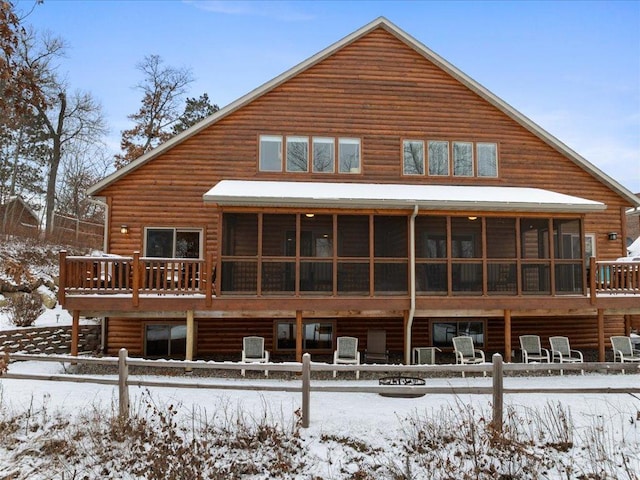 snow covered back of property with a sunroom