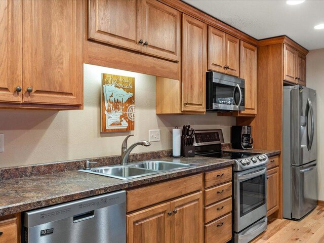 kitchen featuring appliances with stainless steel finishes, light hardwood / wood-style flooring, dark stone countertops, and sink