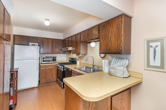 kitchen with sink, light hardwood / wood-style flooring, kitchen peninsula, black gas stove, and white fridge