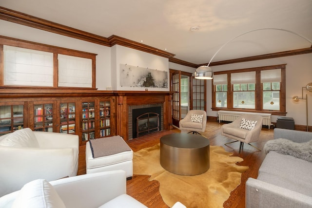 living area with a fireplace, wood finished floors, baseboards, radiator heating unit, and crown molding