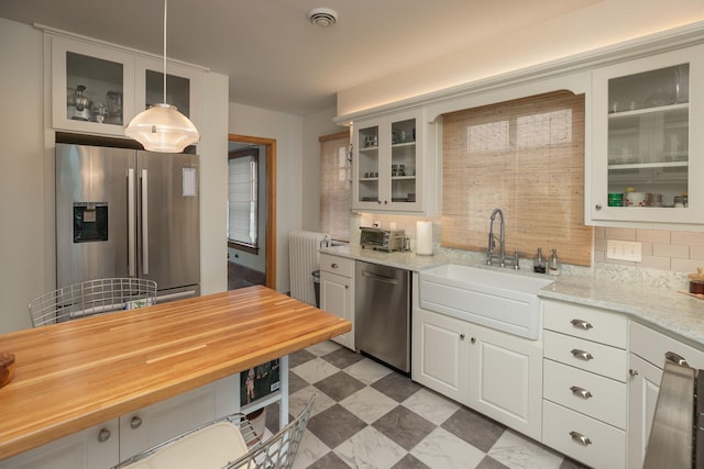 kitchen with dark floors, radiator, decorative backsplash, appliances with stainless steel finishes, and a sink