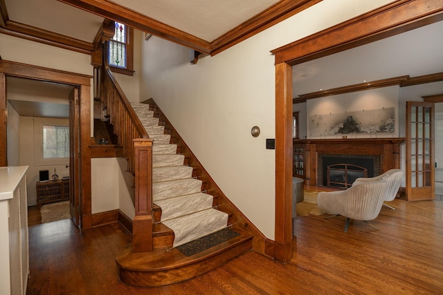 staircase featuring baseboards, wood finished floors, crown molding, french doors, and a brick fireplace