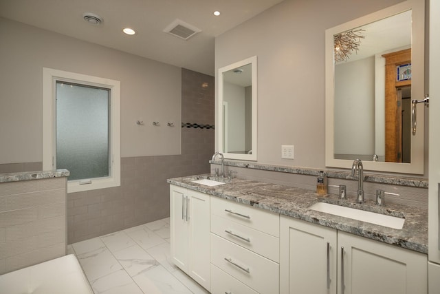 bathroom with marble finish floor, visible vents, tile walls, and a sink