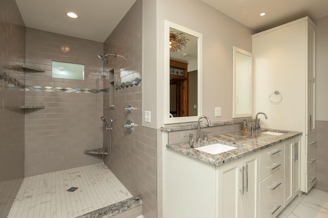 bathroom featuring a tile shower, double vanity, a sink, and recessed lighting