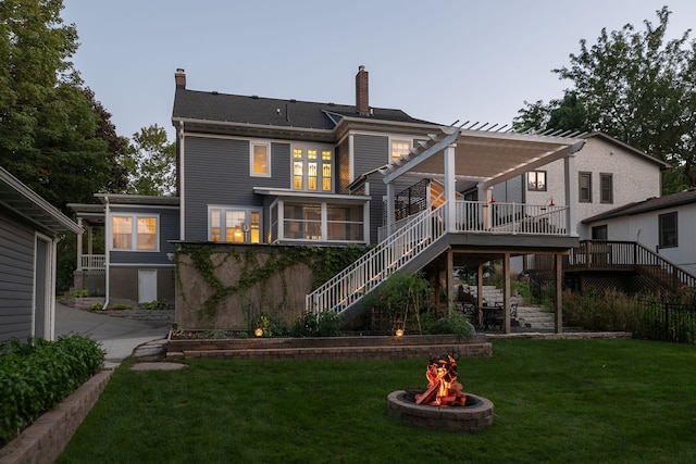 rear view of house featuring a yard, a pergola, a fire pit, a wooden deck, and stairs