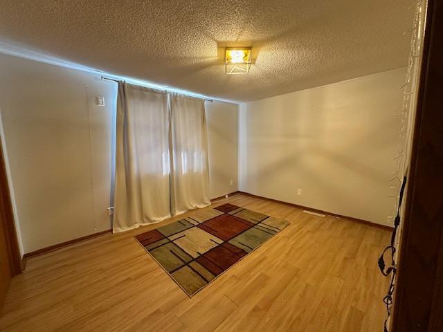 unfurnished room with a textured ceiling, baseboards, and wood finished floors