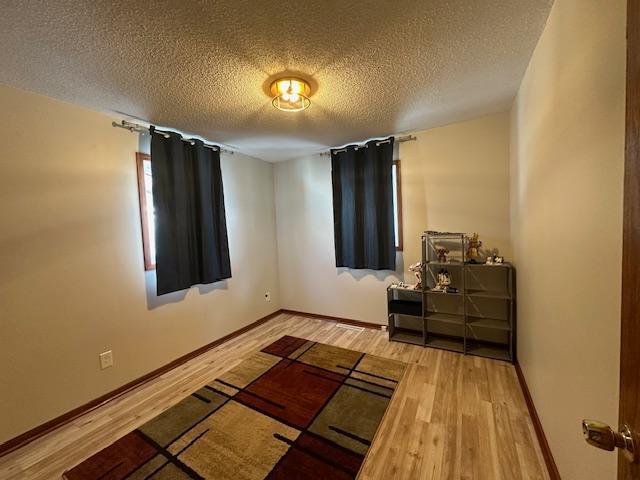 bedroom featuring a textured ceiling, baseboards, and wood finished floors