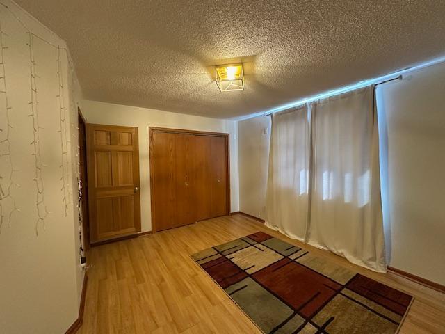 unfurnished bedroom with a textured ceiling, a closet, baseboards, and light wood-style floors