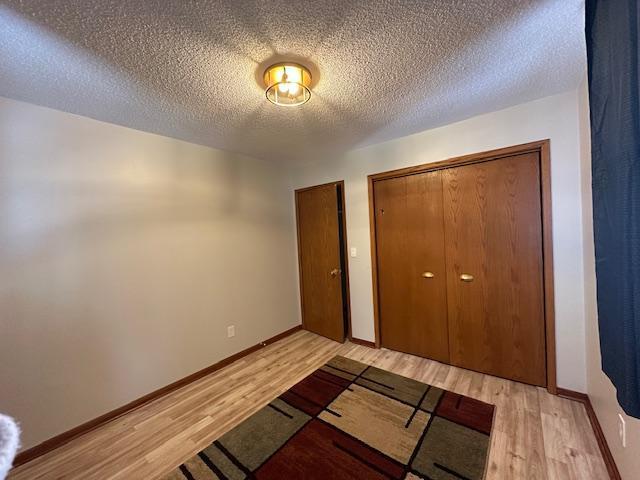 unfurnished bedroom with light wood-type flooring, a closet, a textured ceiling, and baseboards