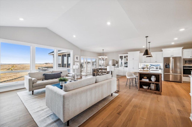 living room with sink, light hardwood / wood-style flooring, lofted ceiling, and a notable chandelier