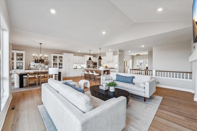 living room with an inviting chandelier, light hardwood / wood-style floors, and vaulted ceiling