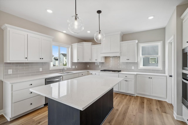 kitchen with a center island, white cabinets, sink, light wood-type flooring, and appliances with stainless steel finishes