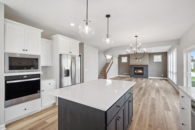 kitchen featuring pendant lighting, white cabinets, light wood-type flooring, a kitchen island, and stainless steel appliances