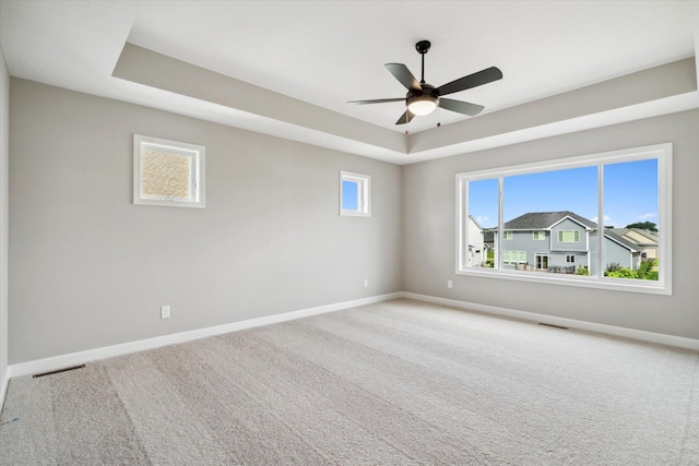 carpeted empty room featuring ceiling fan and a raised ceiling