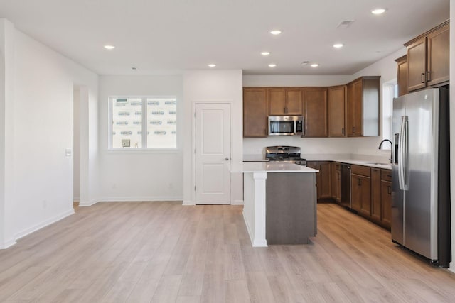 kitchen with appliances with stainless steel finishes, a center island, light hardwood / wood-style floors, and sink