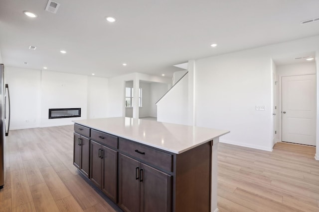 kitchen with stainless steel refrigerator, light hardwood / wood-style flooring, a center island, and dark brown cabinets