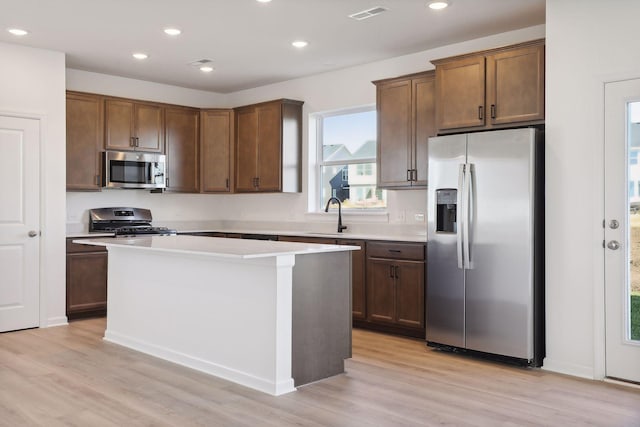 kitchen with sink, a kitchen island, stainless steel appliances, and light wood-type flooring